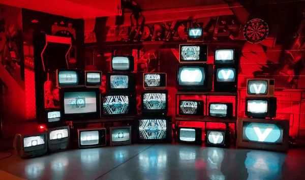 Wall of retro CRT televisions showing the Zyminex logo in a neon-lit room