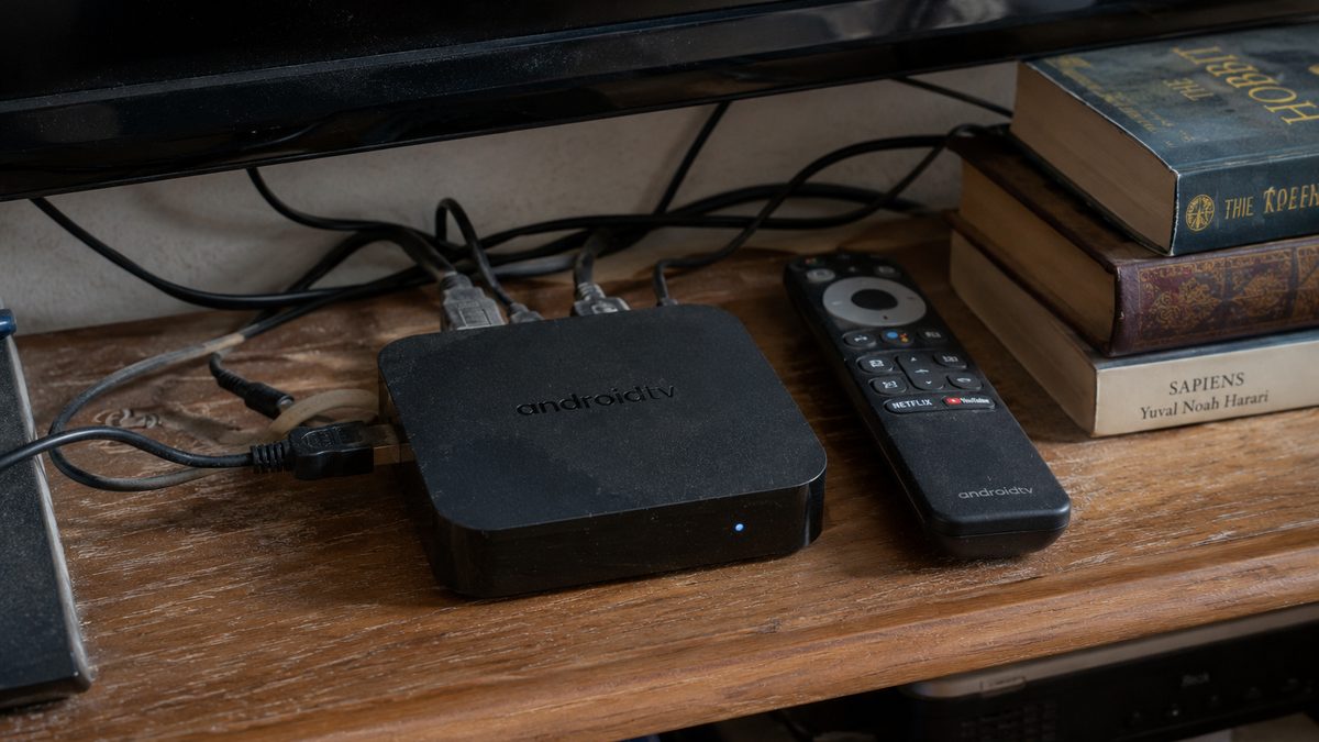 Android TV box and remote control on a shelf beneath a television in a modern living room